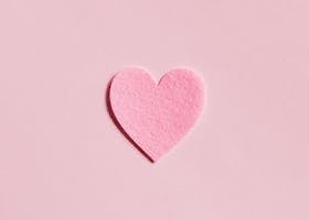 A simple pink felt heart on a light pink background, perfect for Valentine's Day themes.